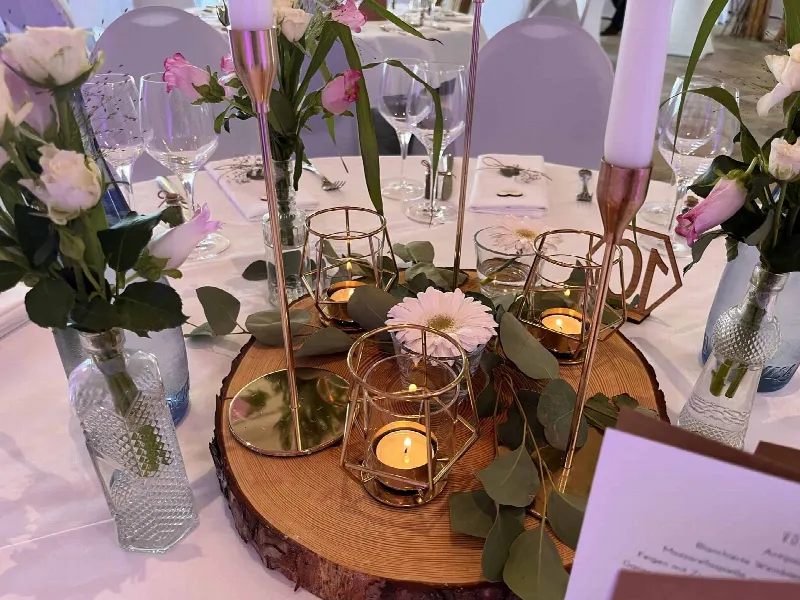Tischdekoration aus Baumscheibe mit goldenen Teelichtern, Kerzen, rosa Rosen und Eukalyptus