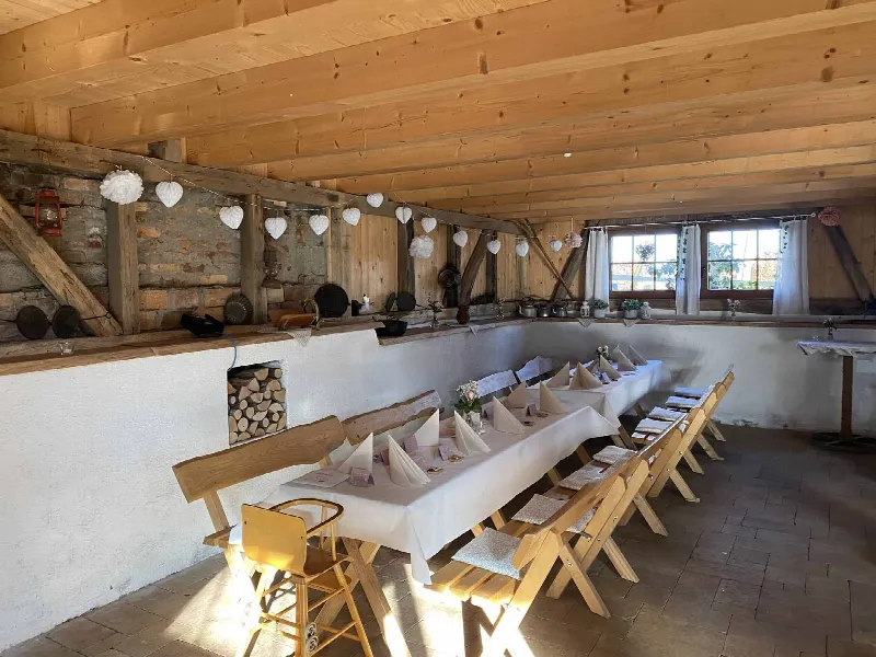 Lange Tafel mit weißem Tuch und Papierherzen-Girlande in einer Scheune mit Holzbalken und Backsteinwand