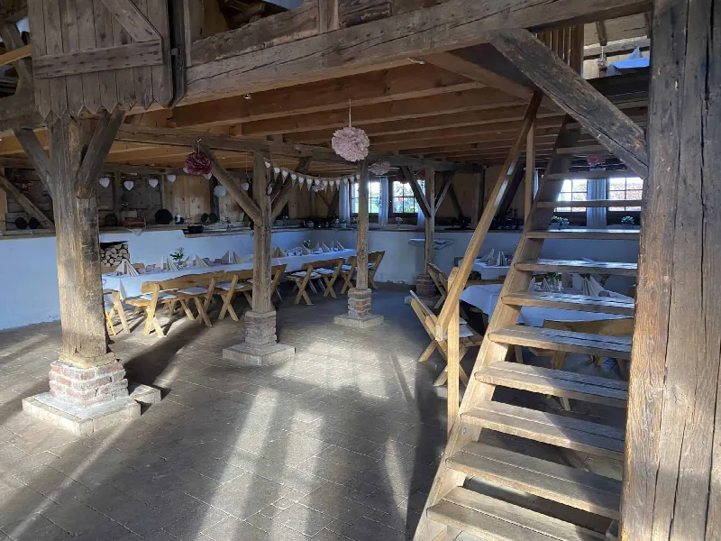 Blick durch die Scheune mit Holztreppe, Pompoms und langen gedeckten Tafeln im Licht der Fenster