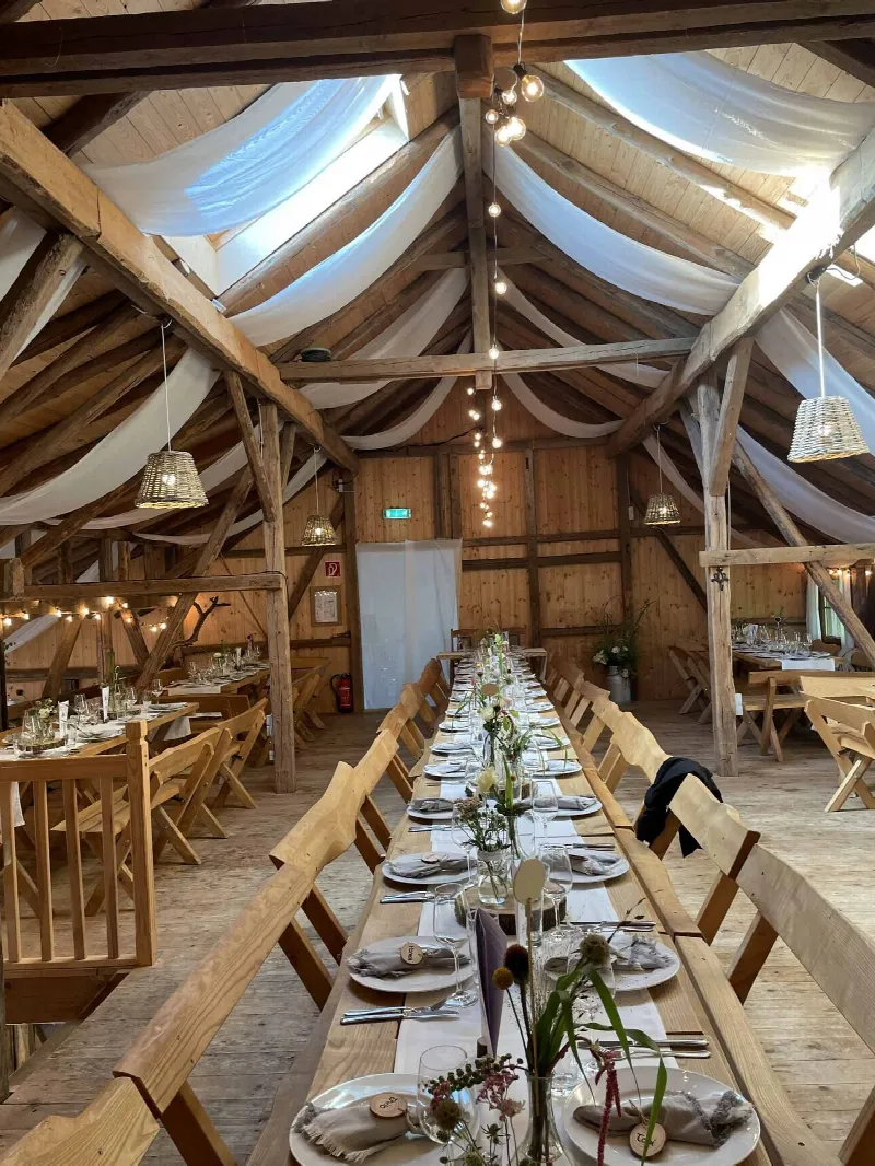 Hochformat der langen Holztafel mit Blumenvasen, darüber der Dachstuhl mit Stoffbahnen und Lichterkette