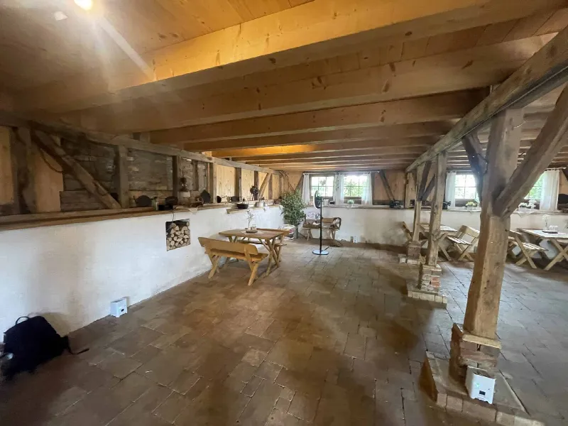 Rustikaler Raum mit Backsteinboden, Holzbalken, Bierbänken und Fachwerk im unteren Geschoss der Scheune