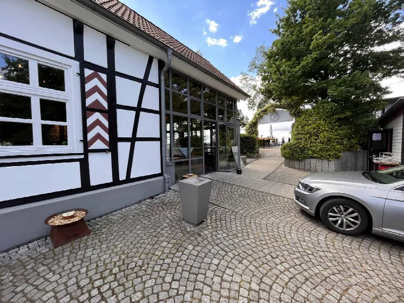 Fachwerkfassade mit gläsernem Anbau, Kopfsteinpflaster und geparktem Auto am Eingang des Jagdhaus Schellenberg