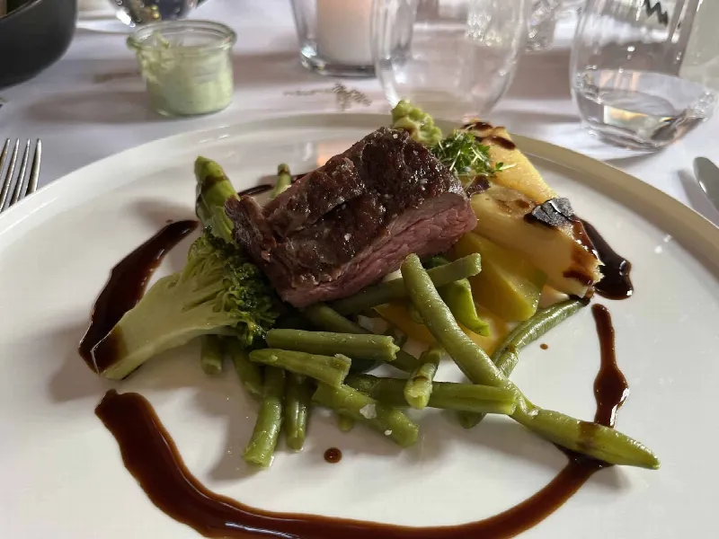 Hauptgang auf weißem Teller mit Rindfleisch, grünen Bohnen, Brokkoli, Kartoffelgratin und dunkler Sauce