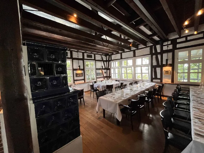 Fachwerksaal mit dunklem Kachelofen im Vordergrund, Holzbalkendecke und eingedeckten Tafeln