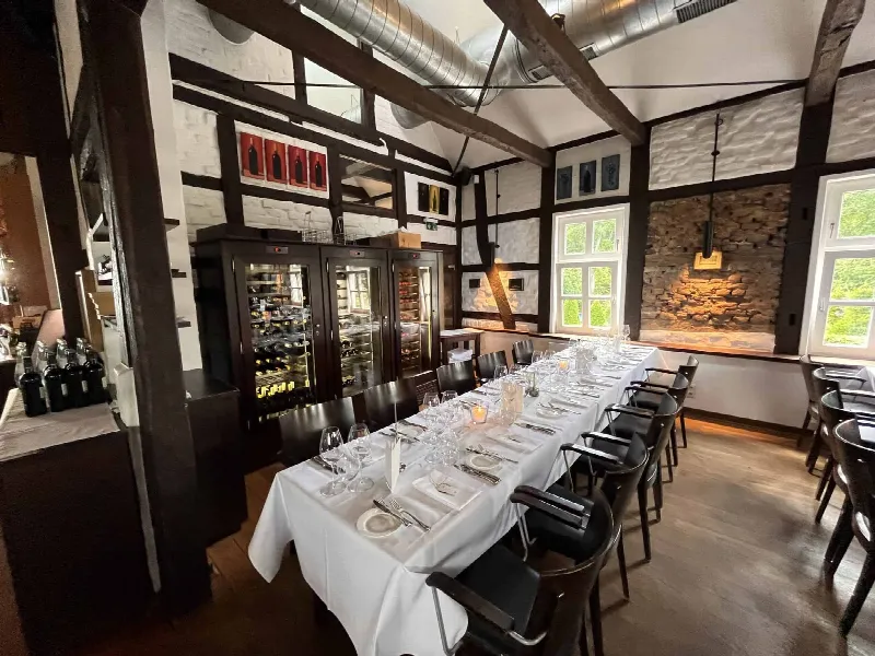 Lange Tafel mit Kerzen im Fachwerksaal, im Hintergrund beleuchteter Weinschrank und Natursteinwand