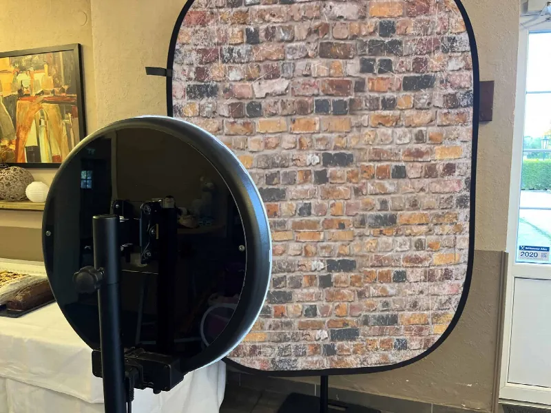 Fotobox mit rundem Spiegel auf Stativ vor einem faltbaren Backstein-Hintergrund im Saal