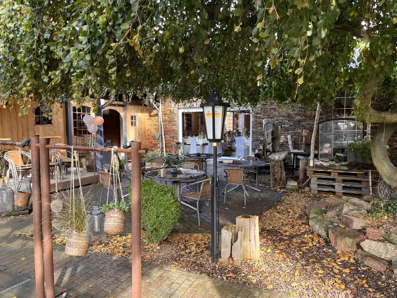 Gartenterrasse mit Bistrotischen unter einer Hängebuche, Backsteinwand und Holzfassade im Herbst