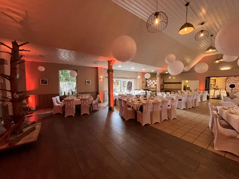 Saal mit weiß gedeckten Tischen, Stuhlhussen und Papierlampen unter der Decke, orangefarbene Wandbeleuchtung
