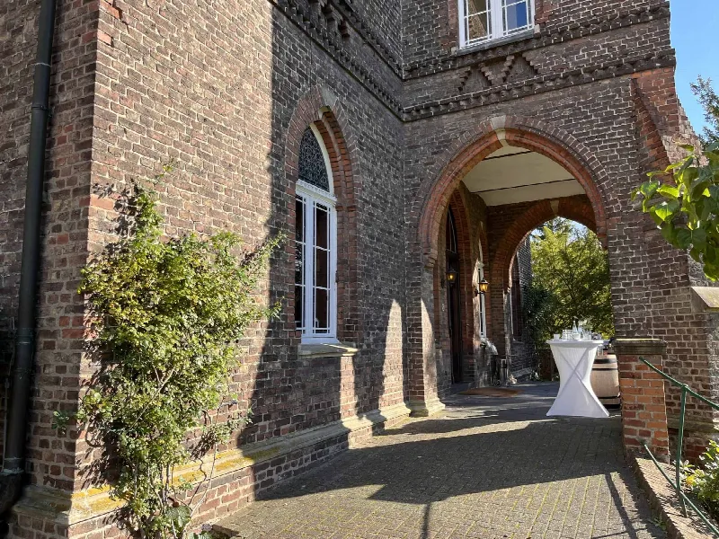 Backsteinarkade mit Rundbogen und Wandlaternen, im Gang ein weiß bezogener Stehtisch mit Gläsern