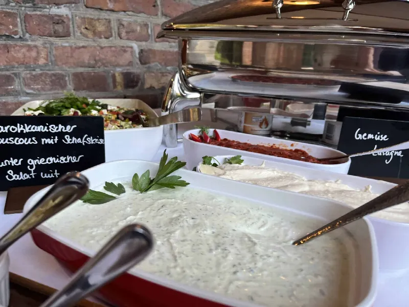 Schalen mit Kräuterdip, Hummus und Salaten, daneben Warmhaltebehälter und Kreidetafeln