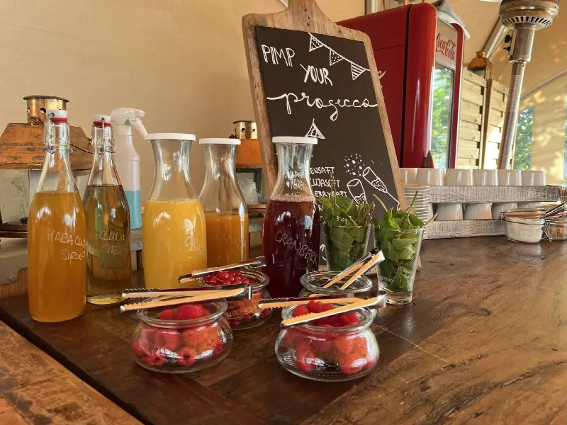 Saftflaschen, Himbeeren und Minze vor einer Kreidetafel „Pimp your Prosecco“ auf Holztheke