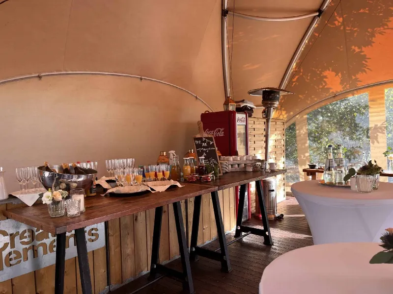 Theke mit Sektschale, Saftgläsern und Tafel „Pimp your Prosecco“, rechts ein Heizpilz und Stehtische