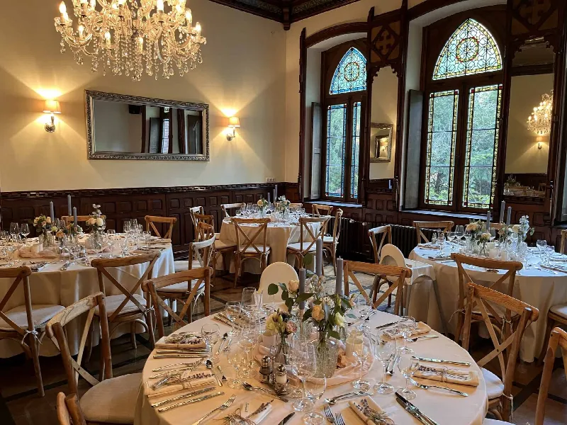 Festsaal mit Kronleuchter, Buntglasfenstern und gedeckten Rundtischen mit Blumen und Kerzen