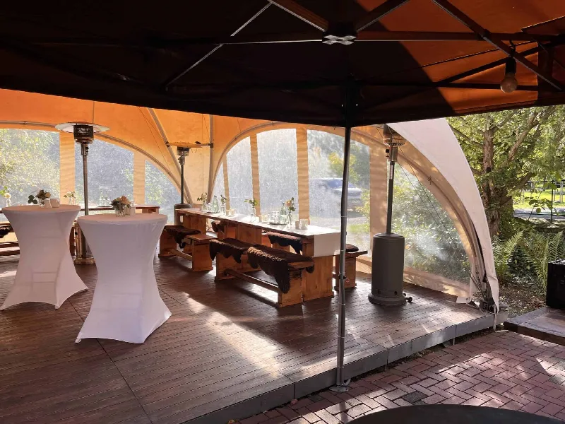 Zeltpavillon mit Holzdielen, langem Holztisch mit Fellauflagen, weißen Stehtischen und Heizpilzen
