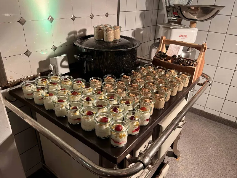 Dessertgläser mit Creme, Trauben und Keksbröseln aufgereiht auf einem alten Herd in der Küche