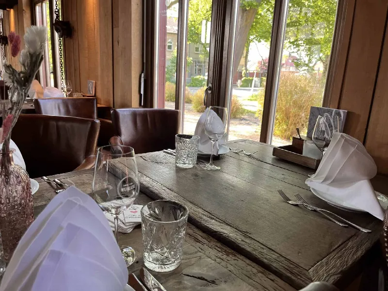 Eingedeckter Holztisch mit Kristallgläsern, gefalteten Servietten und Trockenblumen in rosa Glasvase