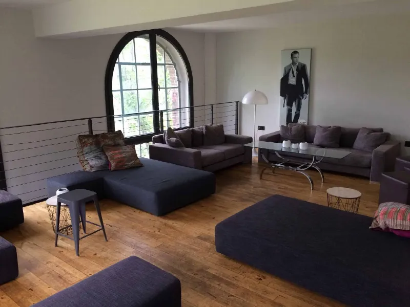 Lounge-Bereich mit dunklen Sofas, großen Polstern und Glastisch vor einem Rundbogenfenster